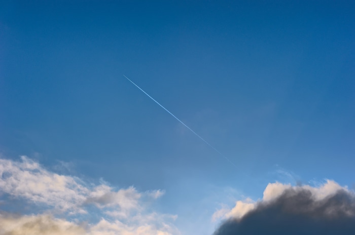 Airplane contrail in a blue sky with clouds