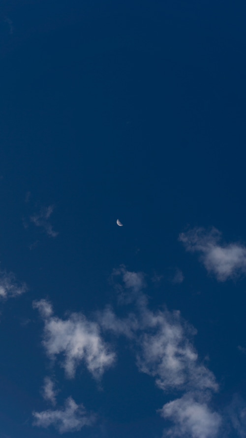 Crescent moon in a deep blue sky with clouds