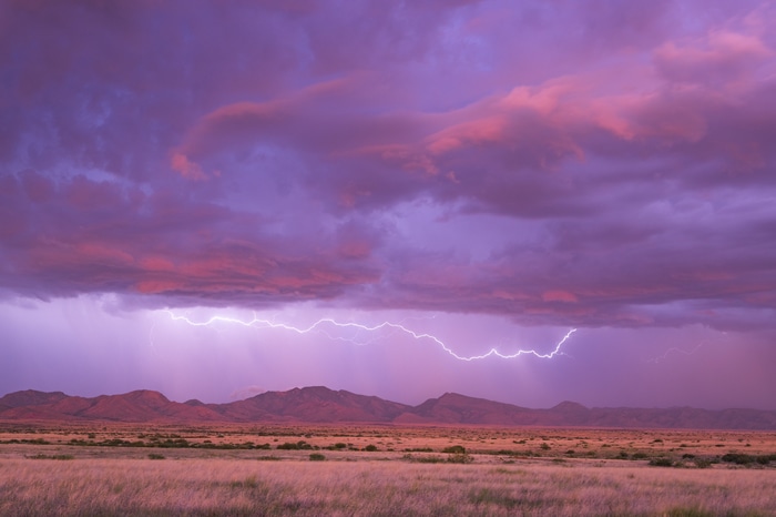 Lightning strikes over desert mountains at sunset