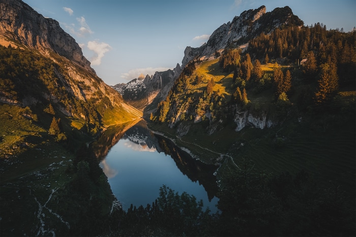 Mountain lake reflection at sunset with forest and waterfall
