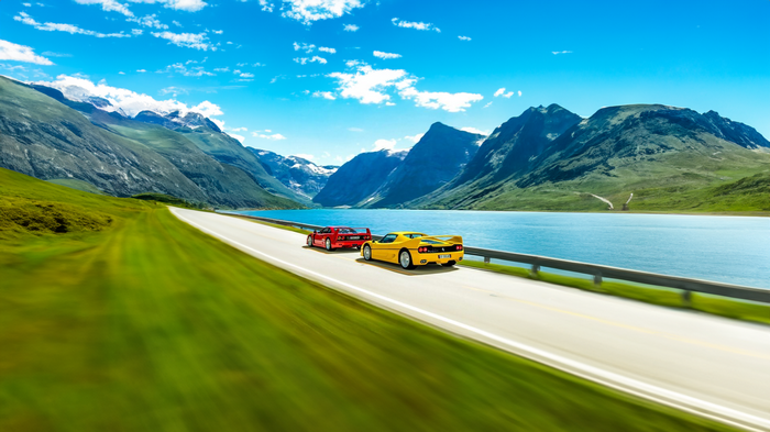 Two Ferrari sports cars driving on a scenic road