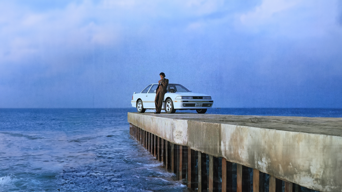 Man leaning on a Toyota car on a jetty by the sea