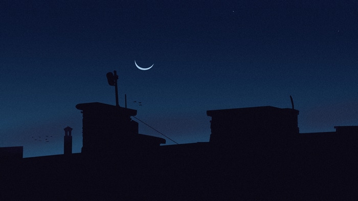 Crescent moon over silhouetted buildings at night