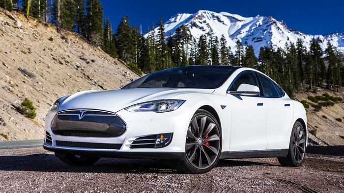White Tesla Model S parked on a gravel road with mountains