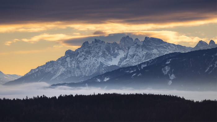 Snow-capped mountains at sunset with clouds and forest