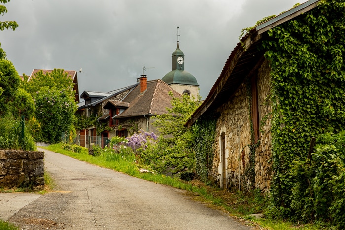 Village road with church and stone building covered in vines