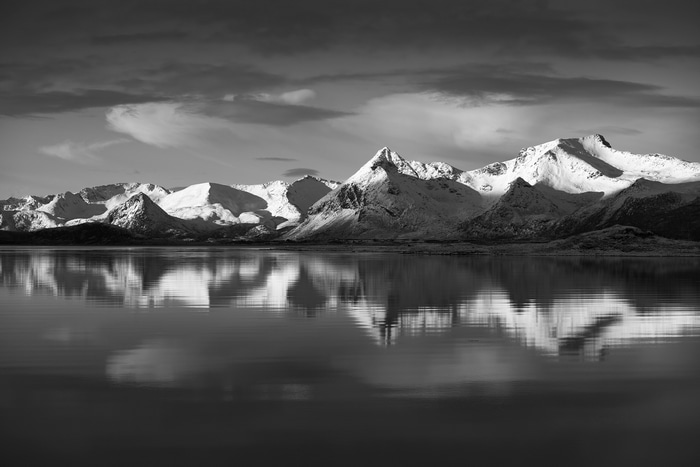 Snow-capped mountains reflected in a calm lake under a cloudy sky