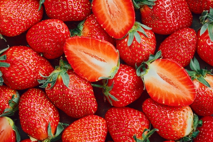 A pile of fresh strawberries, some sliced in half