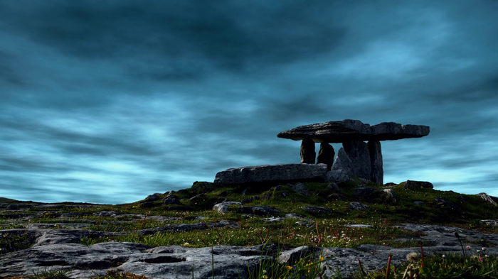 Ancient dolmen structure on a grassy hill under a cloudy sky
