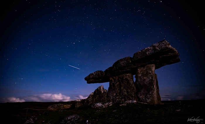 Dolmen under a starry night sky with a meteor