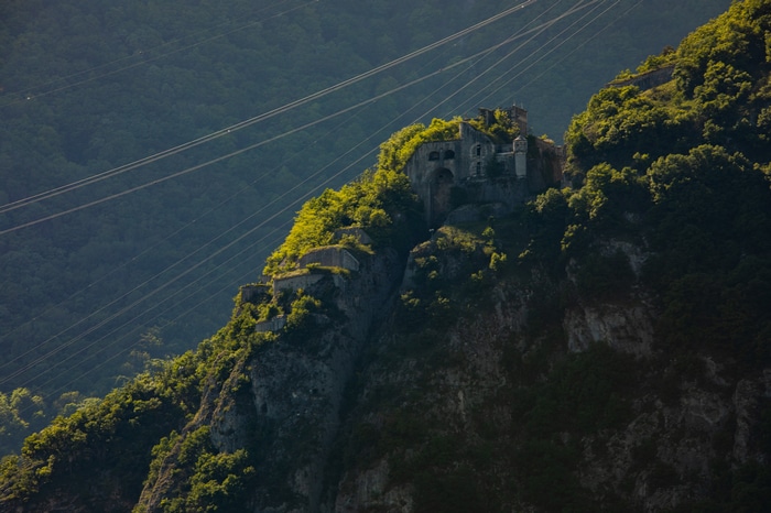 Fortress ruins on a green mountain with power lines