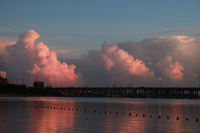 Pink clouds over a bridge and water at sunset