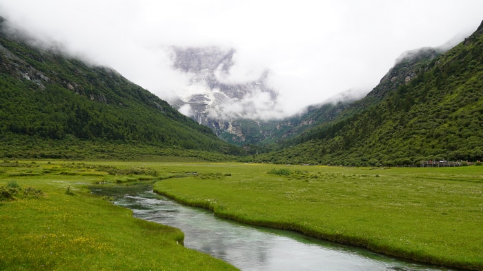 4K river flowing through a grassy valley with mountains and clouds