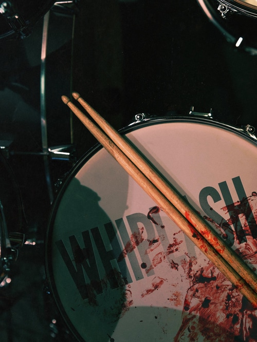 Drumsticks on a drum with "Whiplash" logo and blood