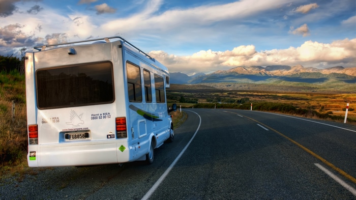 Camper van on a road with mountains and clouds