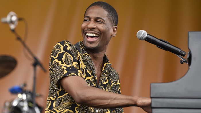 Jon Batiste smiles while playing piano