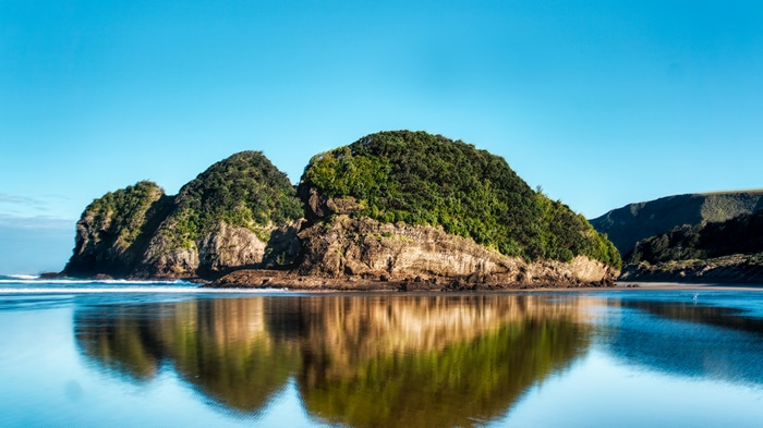 4K reflection of a rocky island covered in green trees