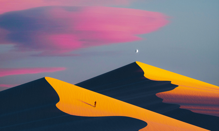 Person walking on sand dunes with moon and clouds