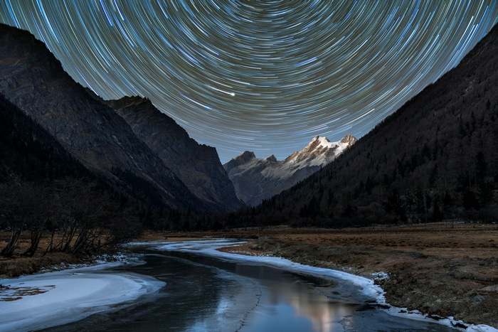 Star trails over snowy peaks and frozen river in Sichuan, China