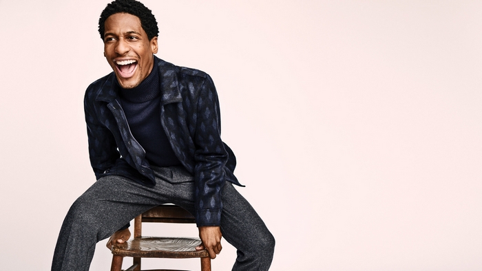 Jon Batiste sitting on a wooden chair