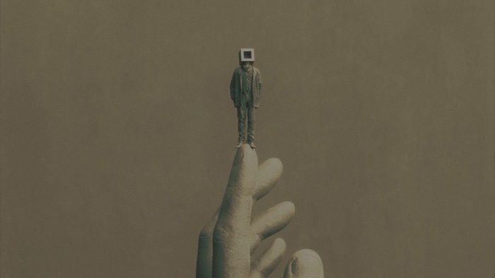 Man with a cube head standing on a giant hand