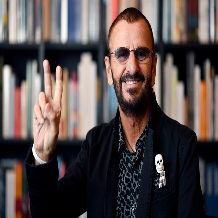 Ringo Starr makes peace sign in front of bookshelf