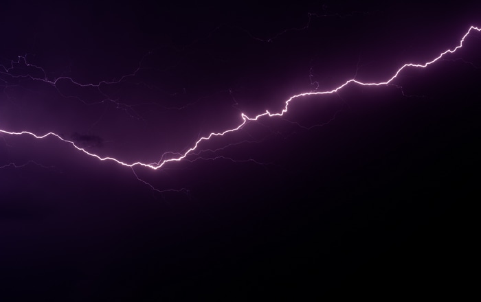 Purple lightning strike against dark sky