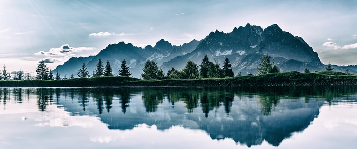 Mountain range reflected in a calm lake with pine trees