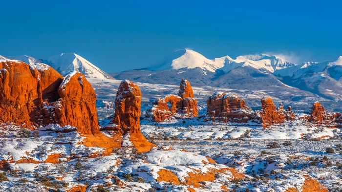 Snow-covered red rocks and mountains under blue sky