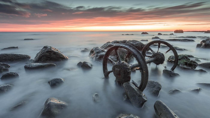 Ruined wheels on a rocky shore at sunset