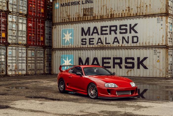 Red Toyota Supra parked near shipping containers