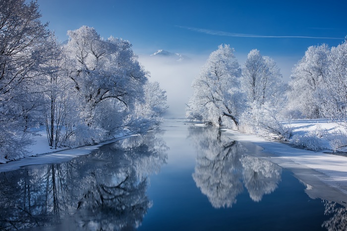 Winter river with snow-covered trees and mountain reflection