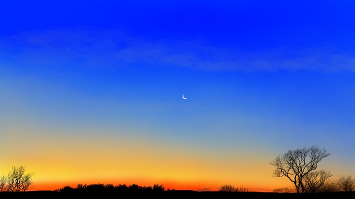 Crescent Moon Over Silhouetted Landscape at Twilight