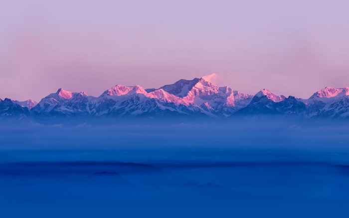 Snow-capped mountains at sunrise over clouds