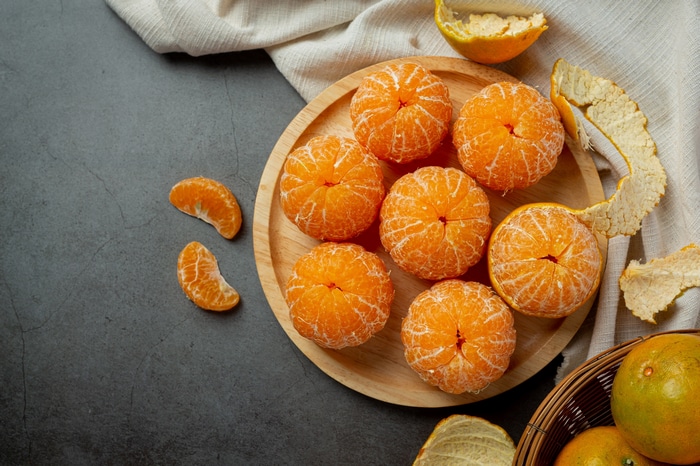 Peeled tangerines on a wooden plate with orange peels