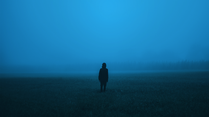 Person standing alone in a foggy field at night