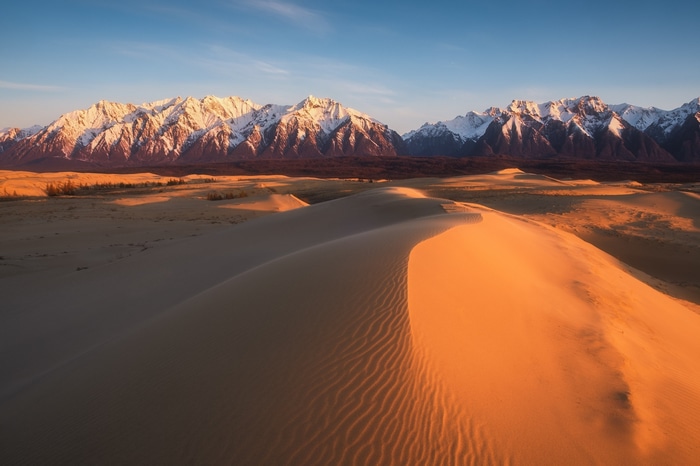 Sand dunes and snow-capped mountains at sunset