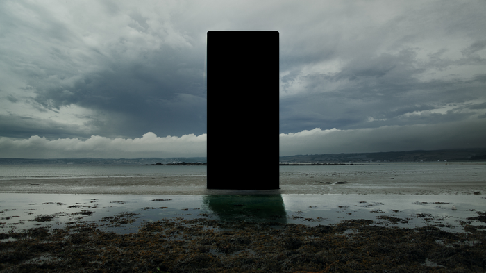 Black monolith on a beach with stormy clouds