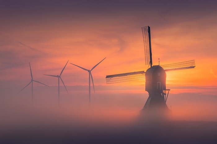 Windmill and wind turbines in mist at sunset