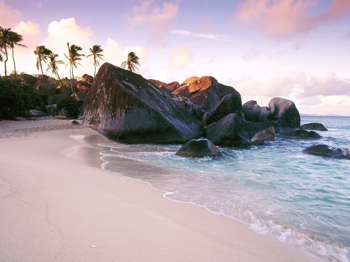 Beach with large rocks and palm trees at sunset