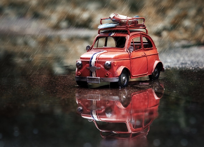 Red toy car with surfboards in the rain