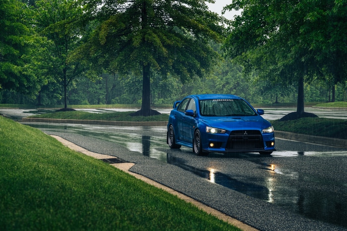 Blue Mitsubishi Lancer Evo X driving on a wet road in the rain