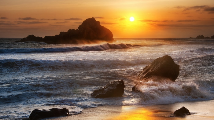 Sunset over the ocean with rocks and waves