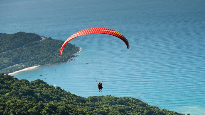 Paraglider flying over a tropical coastline