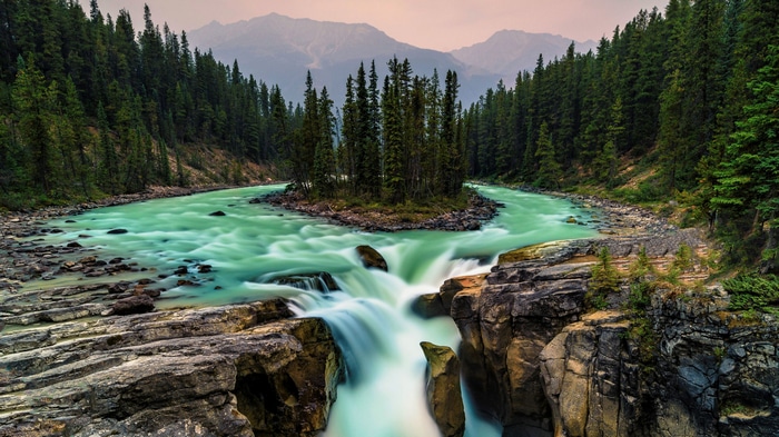 Turquoise river flowing through a forest with mountains