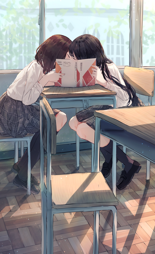 Two schoolgirls kissing over a book in a classroom