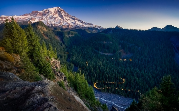 Snow-capped mountain overlooking a winding road through a forest