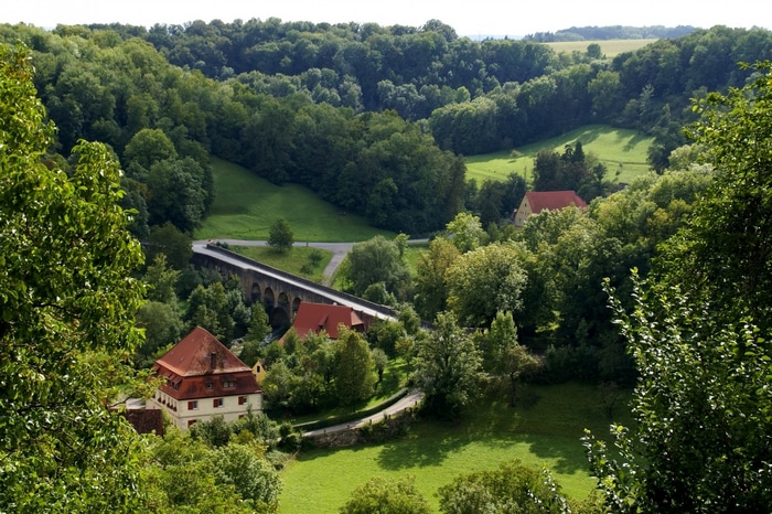 Arched bridge over a valley with houses and forests