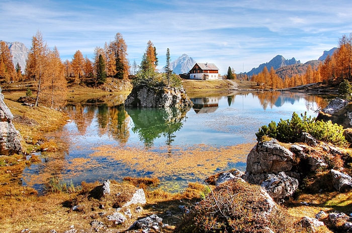 Autumn lake with house and mountains reflection