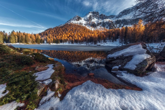 Snow-covered mountains reflected in a partially frozen lake